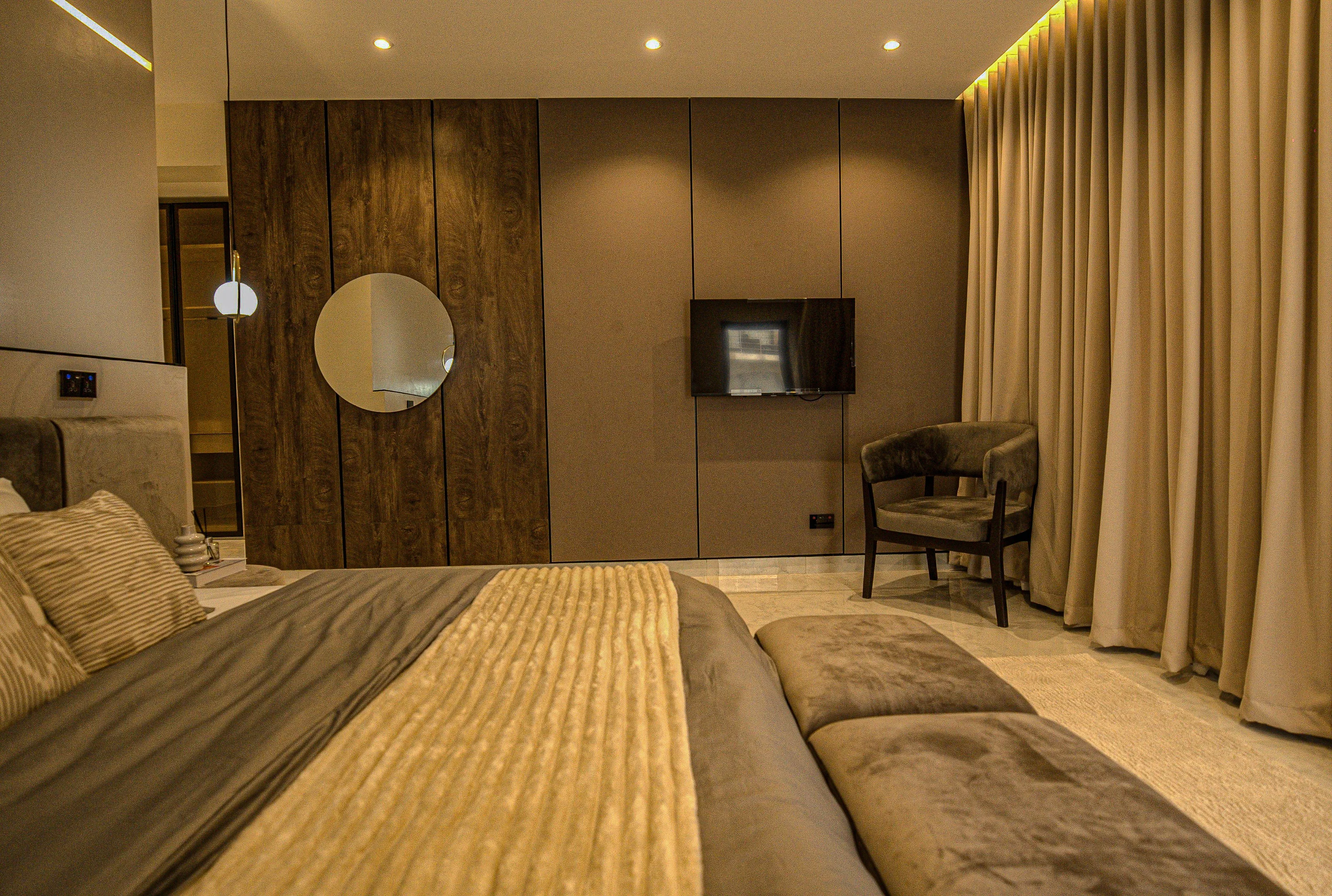 Bedroom with wood-grain panel, circular mirror, television and full-height curtains