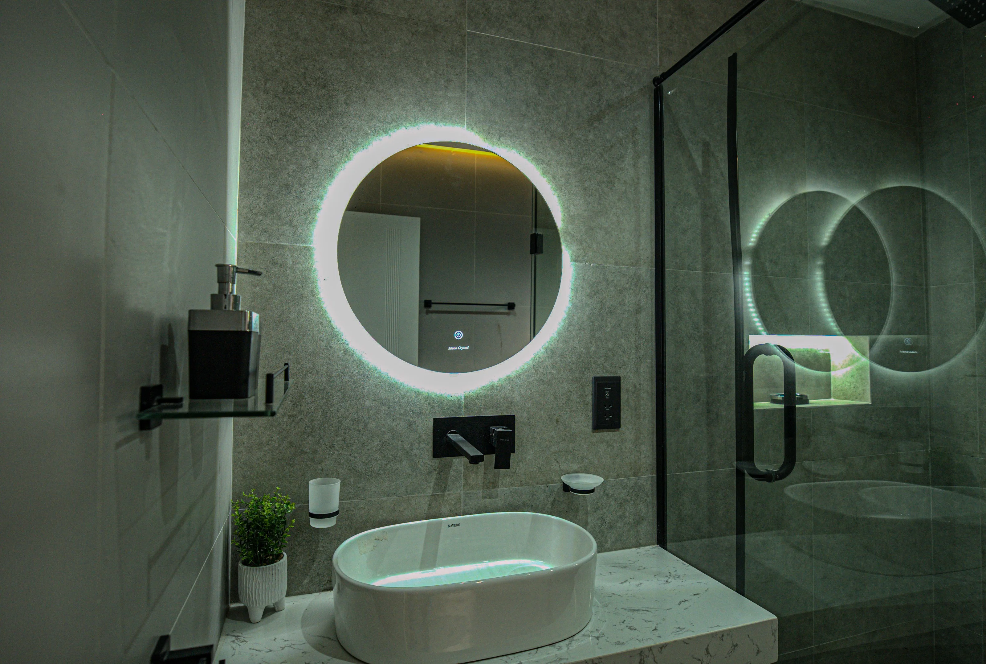 Bathroom basin, illuminated circular mirror, dark fittings and glazed shower enclosure